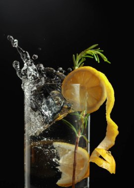 Gin tonic cocktail with lemon and rosemary. Slice of lemon fall in glass with a cocktail. clipart