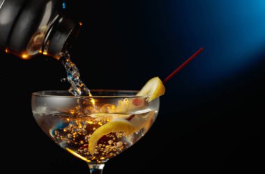 Yeşil zeytinli ve limonlu martini. Kokteyl bardaktan bardağa dökülüyor..