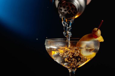 Yeşil zeytinli ve limonlu martini. Kokteyl bardaktan bardağa dökülüyor..