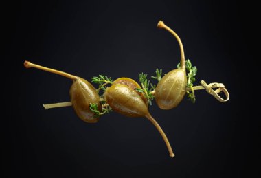 Siyah arka planda kekik olan büyük turşulu konserve kapari..