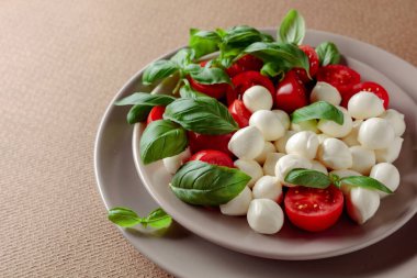 Domatesli Caprese salatası, kahverengi arka planda mini mozzarella ve fesleğen. İtalyan yemeği ve sağlıklı vejetaryen diyeti. 