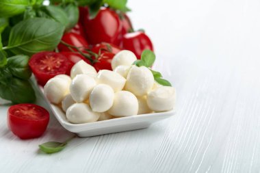 Beyaz ahşap bir masada fesleğenli ve domatesli Mozzarella peyniri. Geleneksel İtalyan atıştırması.