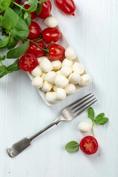 白い木製のテーブルの上にバジルとトマトとモッツァレラチーズ — ストック写真