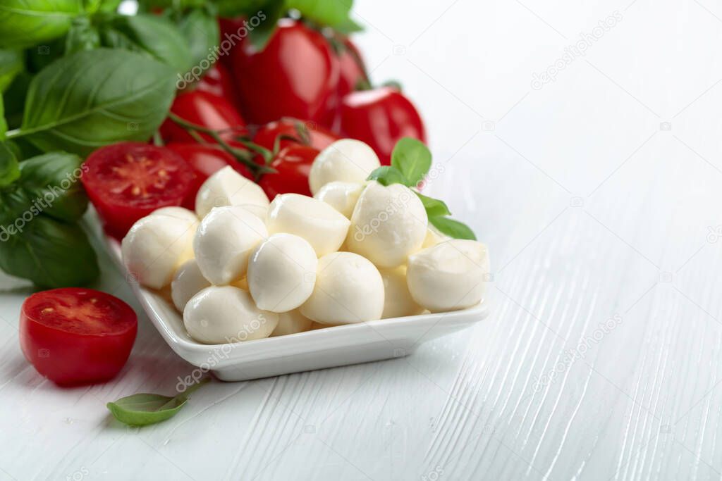 Mozzarella cheese with basil and tomatoes on a white wooden table. Traditional Italian snack.