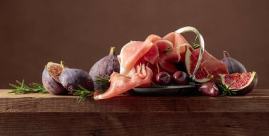 İncirli jambon, biberiye ve eski ahşap bir masada kırmızı zeytin. Boşluğu kopyala.