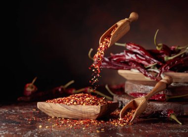 Biberler ahşap bir tabağa dökülür. Kahverengi arka planda kırmızı biber ve kırmızı biber..