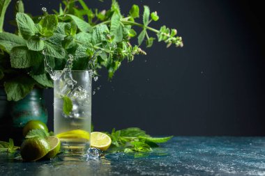 Buzlar mojito ile birlikte dondurulmuş bardağa düşer. Limonlu, naneli ve buzlu yaz içeceği. Kopyalama alanı olan koyu arkaplan.