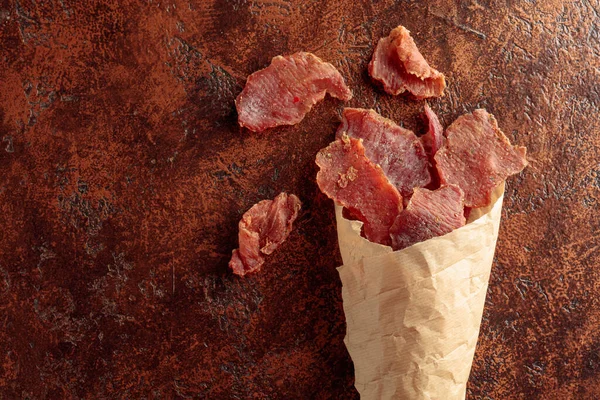 Slices Spicy Dry Cured Meat Paper Bag Old Brown Background — Stock Photo, Image