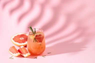 Greyfurtlu, biberiyeli ve buzlu yaz kokteyli. Pembe arka planda, palmiye yaprağı gölgesiyle iç. Yaz, tropikal, taze kokteyl konsepti.