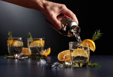 Limonlu ve biberiyeli kokteyl Cin ve Tonik. Barmen bardaktan bardağa kokteyl doldurur..