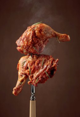 Koyu kahverengi arka planda biberiye serpiştirilmiş ızgara tavuk bacağı. Çatalda tavuk budu..
