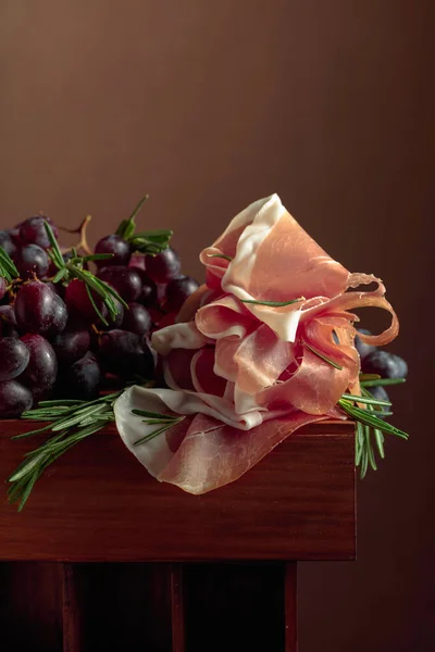 古い木製のテーブルの上にローズマリーとブドウとProsciutto — ストック写真