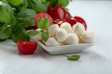 Beyaz ahşap bir masada fesleğen ve domatesli Mozzarella peyniri..