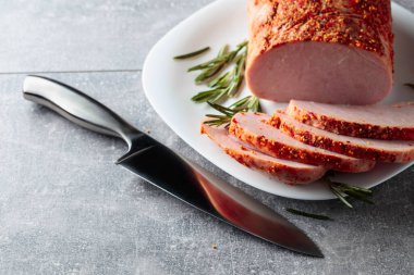 Baharatlı tütsülenmiş jambon, biberiye ve mutfak bıçağı gri bir taş masada..