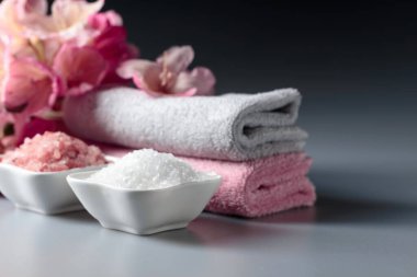 Pembe ve beyaz deniz tuzu, çiçek ve havluyla spa kompozisyonu.