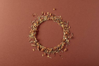 Bitki çayı kahverengi arka plana saçılmıştır. Yuvarlak kopya alanı. Üst görünüm.