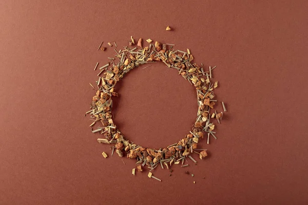 Bitki çayı kahverengi arka plana saçılmıştır. Yuvarlak kopya alanı. Üst görünüm.