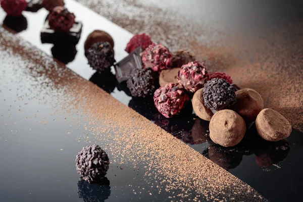 Siyah yansıtıcı arka planda kakao tozu serpiştirilmiş çeşitli çikolatalar..