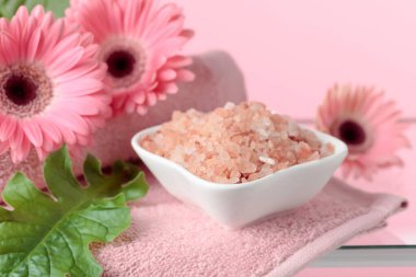 Pembe tuz, çiçek ve havluyla spa kompozisyonu.