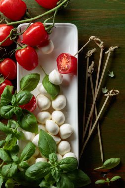 Koyu yeşil ahşap bir masada fesleğen ve domatesli Mozzarella peyniri. Üst görünüm.