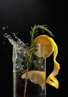 Gin tonic cocktail with lemon and rosemary. Slice of lemon fall in glass with a cocktail. clipart