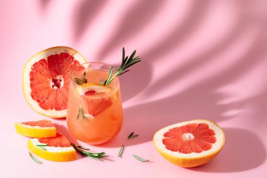 Greyfurtlu, biberiyeli ve buzlu yaz kokteyli. Pembe arka planda, palmiye yaprağı gölgesiyle iç. Yaz, tropikal, taze kokteyl konsepti.