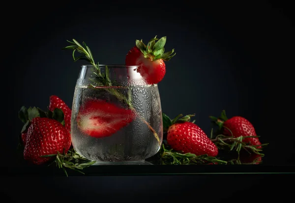 Cocktail gin tonic with ice, strawberries, and rosemary in a frozen glass.
