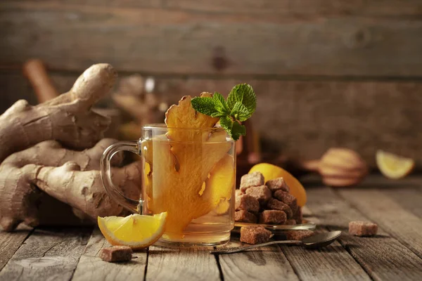 Ginger tea with ingredients. Ginger, lemon, mint and brown sugar on an old wooden table.