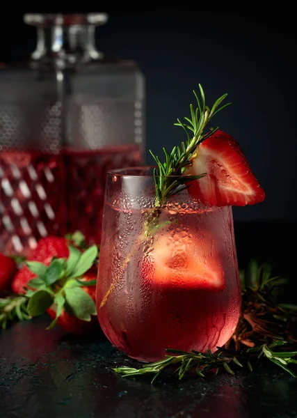 Cocktail gin tonic with ice, strawberries, and rosemary. Refreshing drink with natural ice in a frozen glass.