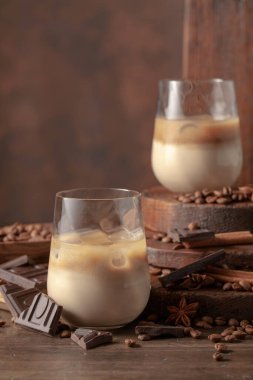 Eski ahşap arka planda buzlu bardakta İrlanda kreması ve kahve kokteyli. Kahve çekirdekleri, tarçın, anason ve çikolata parçaları masaya saçıldı.. 