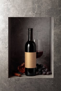 Mavi üzümlü bir şişe ve bir bardak kırmızı şarap. Şişede eski boş etiket var. Boşluğu kopyala.