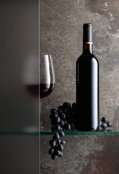 Bottle and a glass of red wine with a bunch of grapes. The still life is partially covered by a frosted glass door.  Copy space.