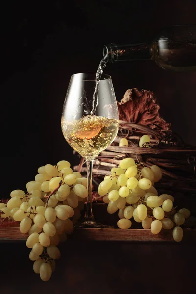 Wine is poured into a glass. White wine and bunch of grapes on vintage wooden table.