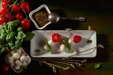 Koyu yeşil ahşap bir masada fesleğen ve domatesli Mozzarella peyniri. Üst görünüm.