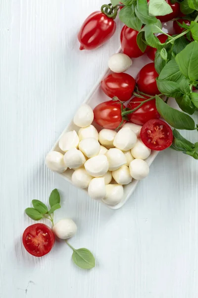白い木製のテーブルの上にバジルとトマトとモッツァレラチーズ — ストック写真