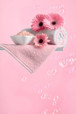 Pembe baloncuklu pembe arkaplan üzerinde pembe tuz, çiçek ve havlu içeren spa kompozisyonu.