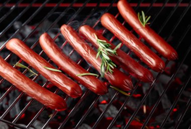 Izgarada ızgara sosis ve siyah arka planda duman..