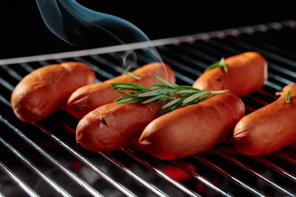 Grilled sausages on a grill with smoke on dark background.