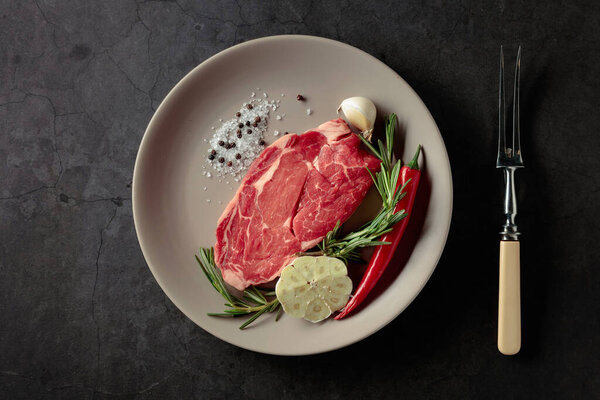 Raw beef meat steak for grilling with rosemary, garlic, salt, and pepper. Top view.