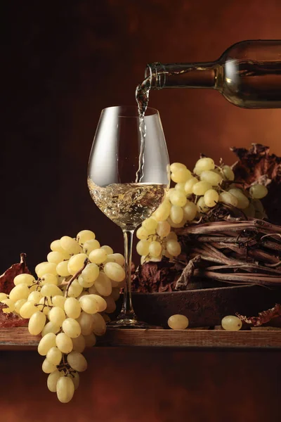 Wine is poured into a glass. White wine and bunch of grapes on vintage wooden table.