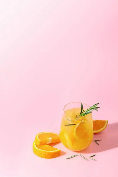 Summer cocktail with orange, rosemary, and ice. Drink on pink background with copy space. Summer, tropical, fresh cocktail concept.