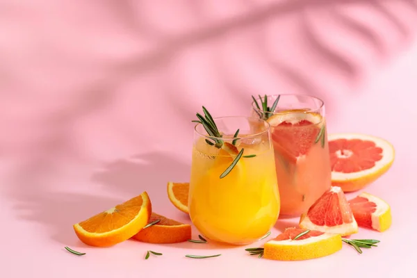 Summer cocktails with grapefruit, orange, rosemary, and ice. Drinks on pink background with palm leaf shadow. Summer, tropical, fresh cocktail concept.