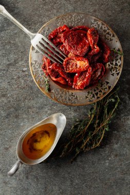 Zeytinyağında güneşte kurutulmuş domatesler ve eski bir taş masanın üzerinde kekik. Üst görünüm.