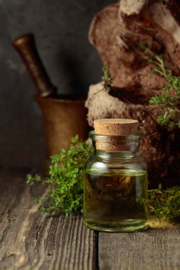 Bottle of thyme essential oil with fresh thyme twigs on an old wooden table.