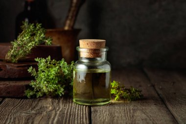 Bottle of thyme essential oil with fresh thyme twigs on an old wooden table.
