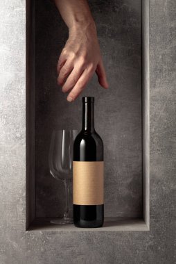 Bottle of red wine. On the bottle old empty label. Hand reach for a bottle of wine.