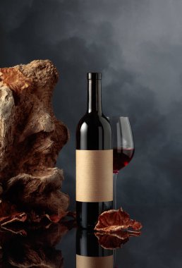 Eski etiketli bir şişe kırmızı şarap. Arka planda eski dallar, kurumuş asma yaprakları ve karanlık bulutlu bir gökyüzü. Metnin için alanı olan ön görünüm.