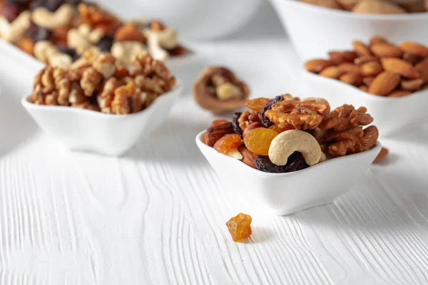 Mix of nuts and raisins on a white wooden table. Presented raisins, walnuts, hazelnuts, cashews, pecans, and almonds.