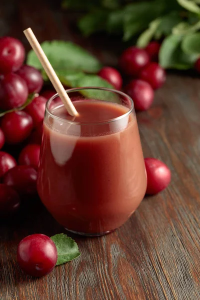 Red plums and a glass of plum juice on a wooden table.