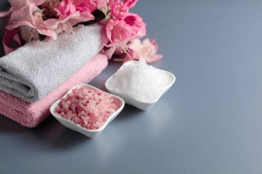 Spa composition with pink and white sea salt, flowers, and towel. Copy space.